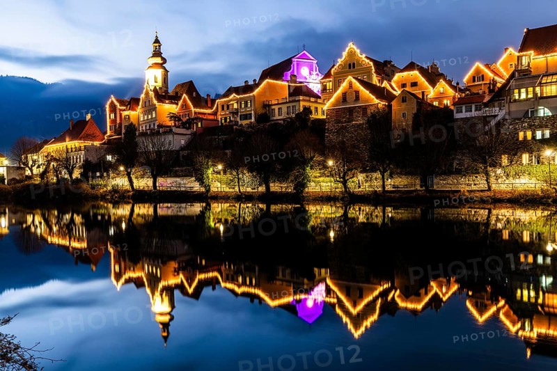Christmas illuminated house facade of Frohnleiten reflected in the river Mur, blue hour, Frohnleiten, Styria, Austria, Europe
