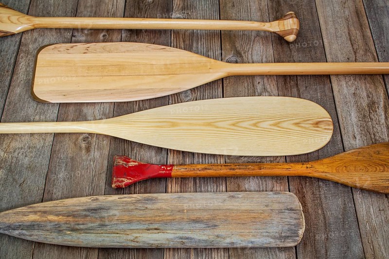 Old and new wooden canoe paddles on a wood deck