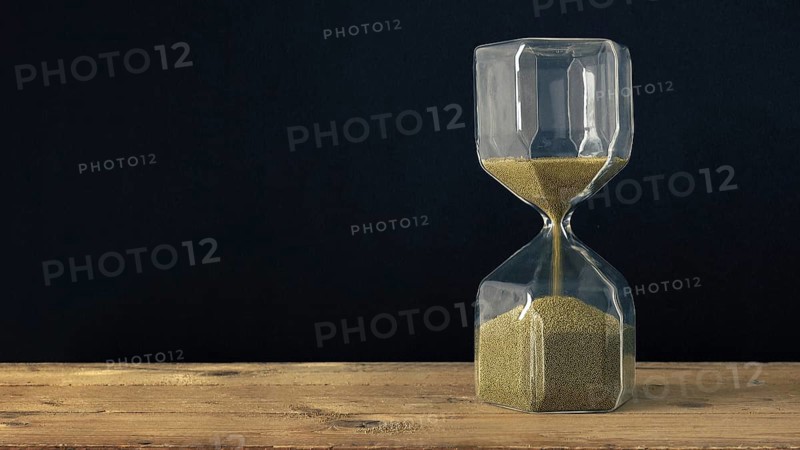 An image of a hourglass on a wooden underground with black background