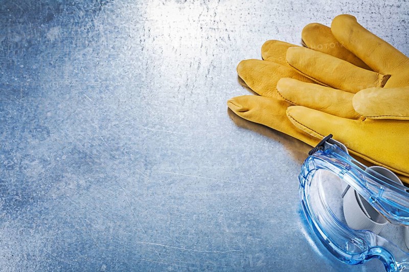 Assortment of safety glasses gloves on metallic background construction concept