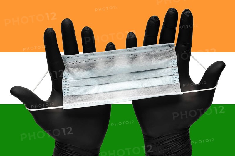 Doctor holds face mask in hands in black medical gloves on background colors National Flag of India. Pandemic insurance coronavirus, flu, airborne diseases. Human medical respiratory mask