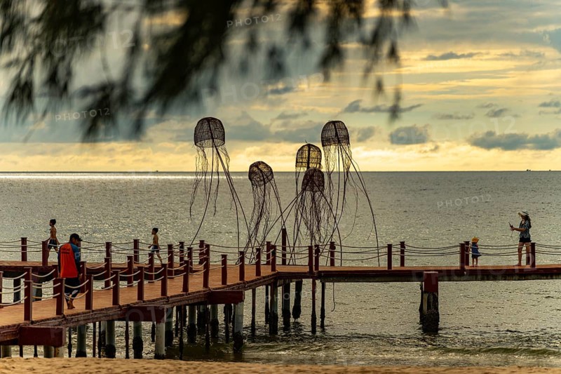 Families walking on a pier with jellyfish sculptures at a peaceful ocean sunset, sun, sunset, beach, sand, sculpture, clouds, Sunset Sanato Beach in Phu Quoc island in Vietnam