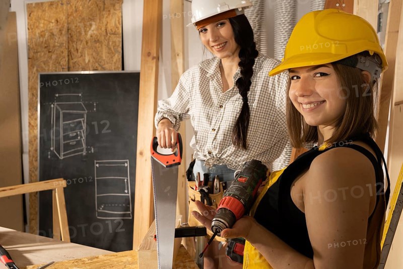 Two smiling girls ready to start work on a construction site. Blonde and dark haired. A lady engineer and a young employee in training