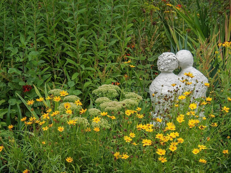 Stone sculpture in the middle of a blooming garden landscape with yellow flowers and green foliage, borken, münsterland, germany