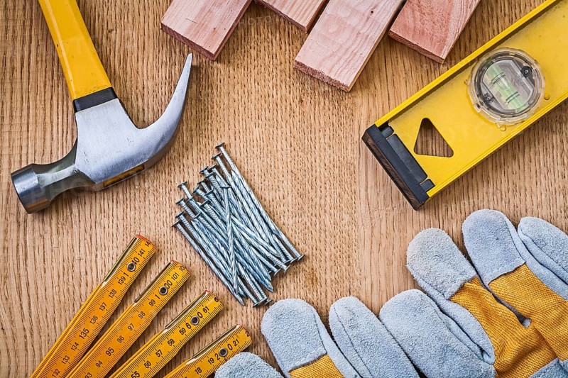 Set of tools claw hammer stack of nails safety gloves construction level wooden meter planks on wooden board