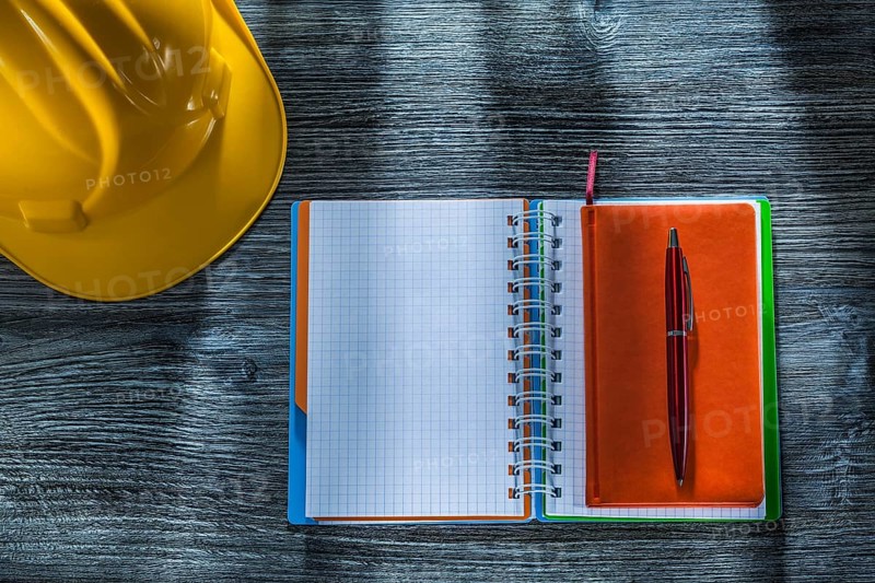 Spiral notepad pen building helmet on wooden board
