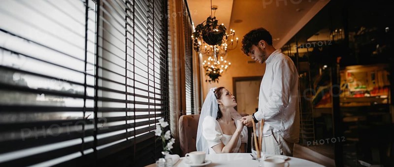 Bride and groom sharing a romantic moment by the window in a softly lit cafe