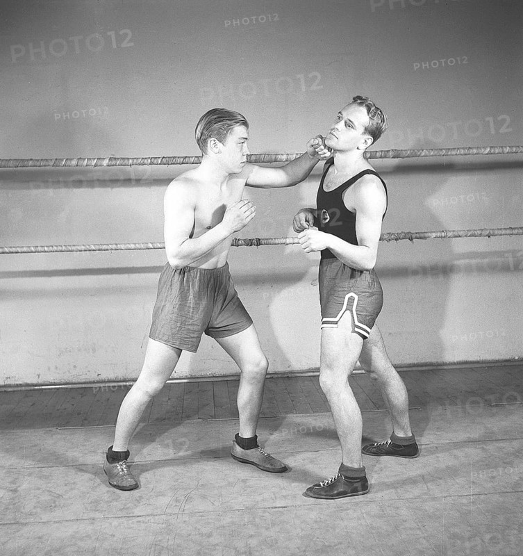 Boxing in the old days. Two young boxers facing each other, dressed for boxing but lacking boxing gloves. One boxer has completely lost his guard and the opponent is quick and lands a left hook to the cheek. Sweden 1944 Kristoffersson ref K116-3