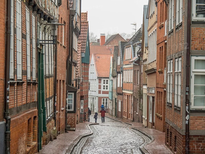 Cobbled street in an old town with historic half-timbered houses and two walkers, stade, germany