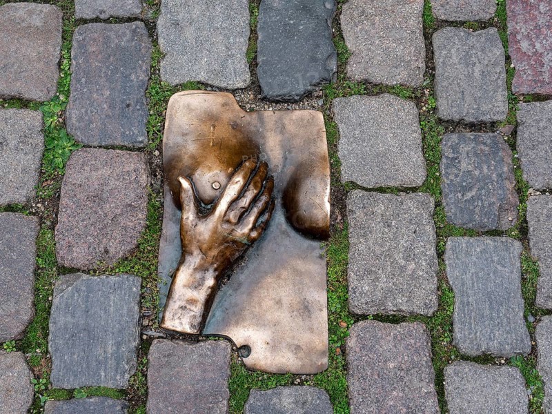 Bronze relief of a hand embracing a female breast on the ground, between granite paving stones in the Oudekerksplein in front of the Oude Kerk in the Red Light District of the historic centre of Amsterdam, North Holland, Netherlands