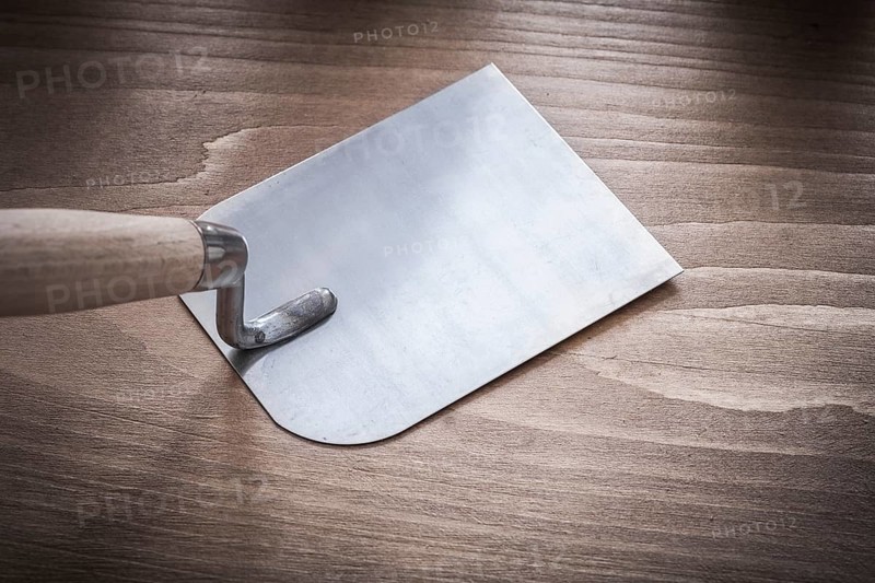 Metal bricklaying trowel on vintage wood board close up view