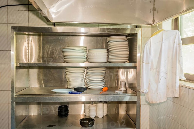 Stacks of dishes on stainless steel storage rack in abandoned resort restaurant kitchen