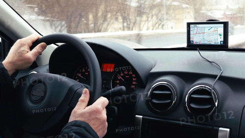 Close-up shot of a man driving a car in winter city. GPS device on the dashboard helps him to find the way