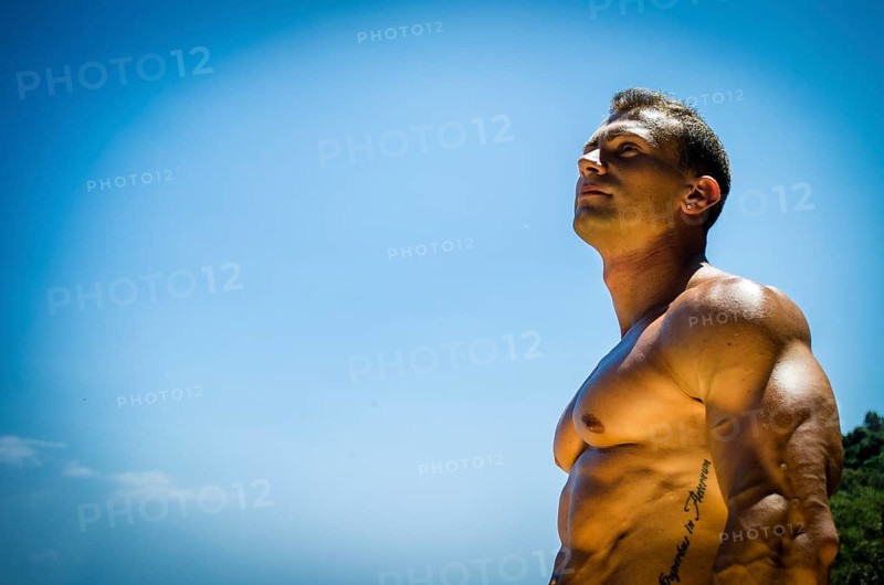 Handsome young muscle man at the seaside, outdoors, showing muscular pecs and torso in front of the sea