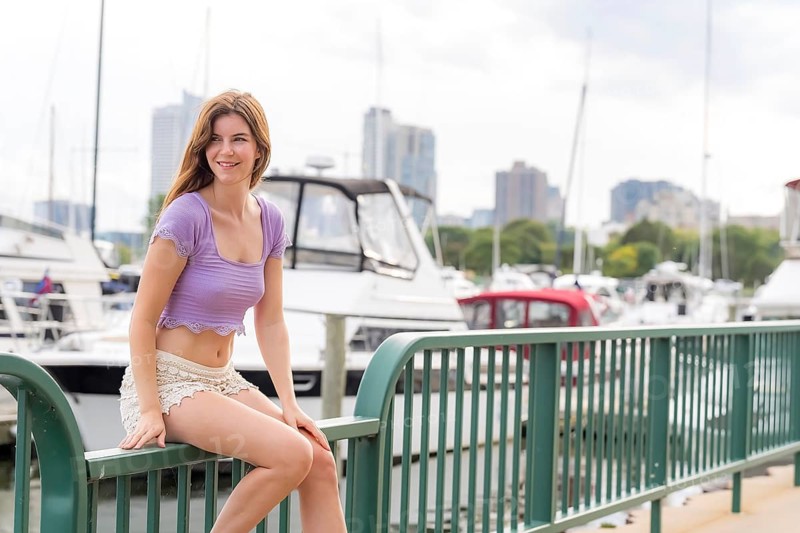 A gorgeous redhead model enjoys the perfect summer weather at a local marina, surrounded by boats of all kinds in the background, their reflections dancing on the water under the bright, sunny sky, Milwaukee, United States of America