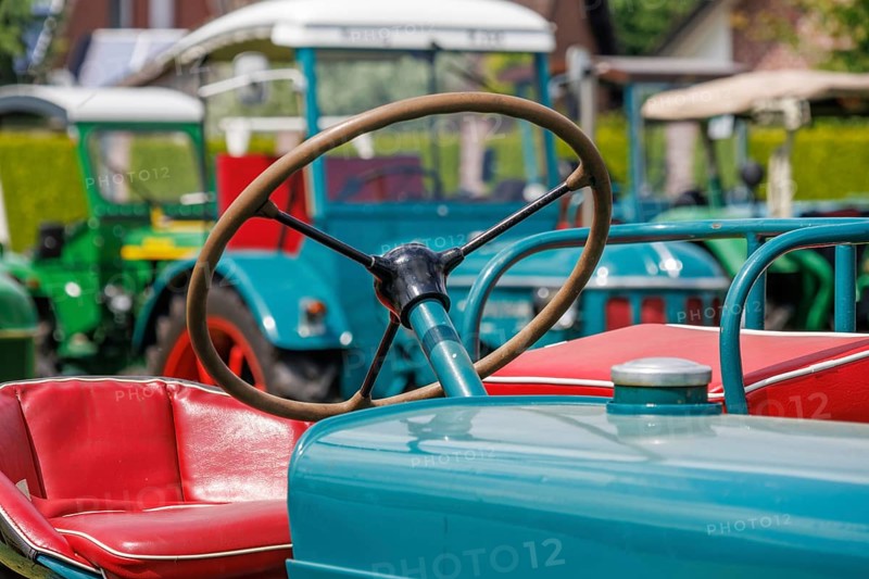 Detail of a tractor with red seat and steering wheel in the foreground, südlohn, münsterland, germany