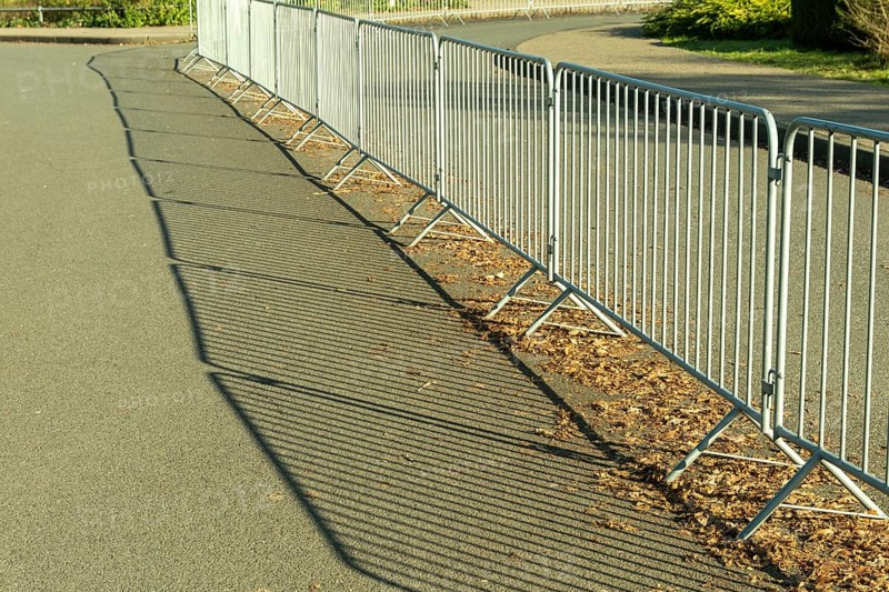 Metal crowd control barriers casting long shadows on an asphalt road