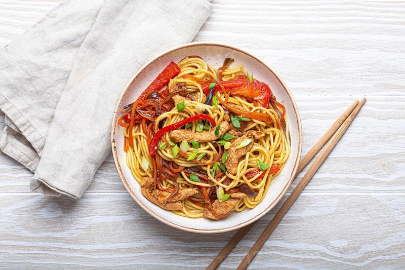 White bowl with Chow Mein or Lo Mein, traditional Chinese stir fry noodles with meat and vegetables, served with chopsticks top view on rustic white wooden background table, food photography, food photography