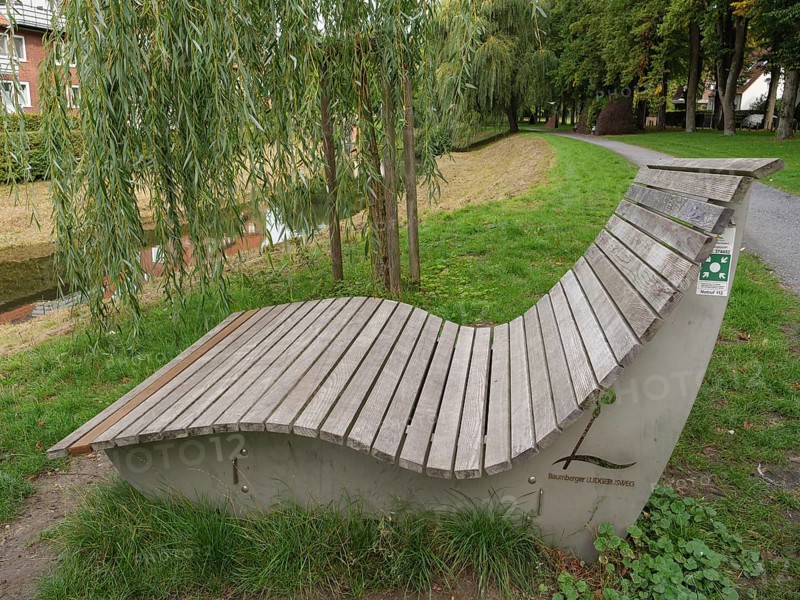A curved wooden bench stands under a willow tree along a park path, suitable for relaxation, Coesfeld, münsterland, germany