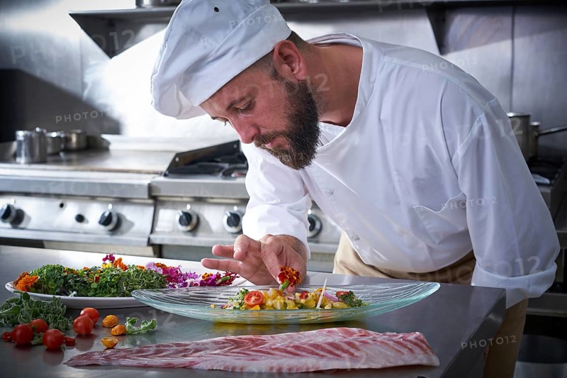 Chef garnishing flower in ceviche dish with hands at stainless steel kitchen