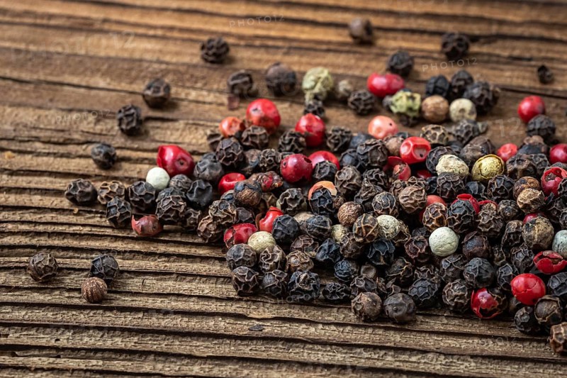 Peppercorns on dark rustic wooden background. Mix of different peppers