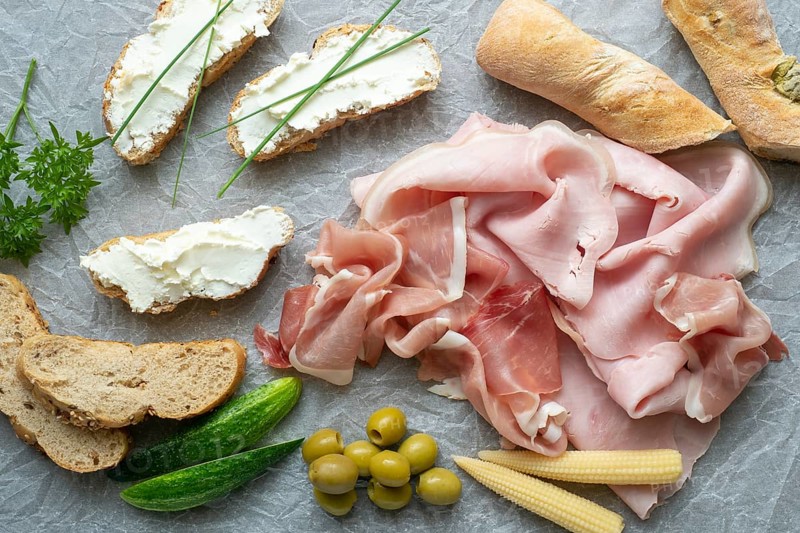 Cold appetizer. Cold cuts. Different snacks on a white crumpled paper, ham, bread, vegetables, from above