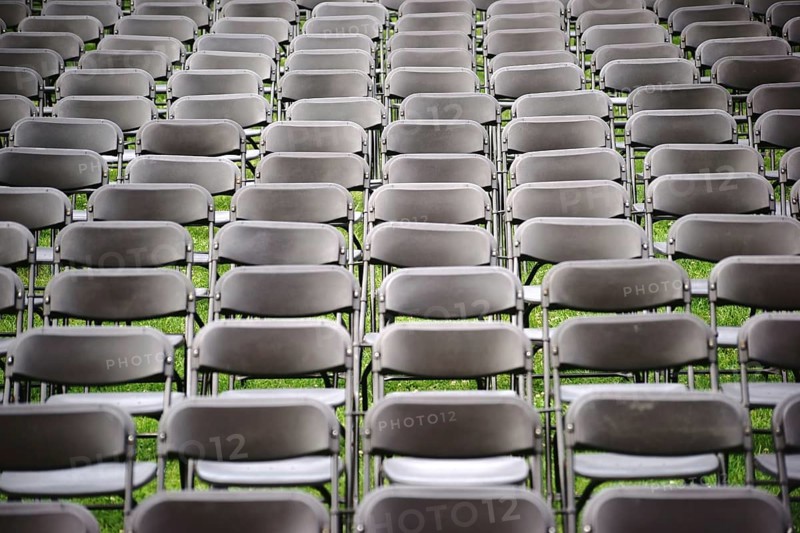 Parallel rows of empty folding chairs in a meadow in front of a concert