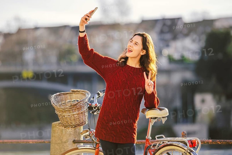A beautiful young woman with a retro red bicycle is making a photo of herself in the old city of Europe on the River Rhine embankment in the Swiss city of Basel. Sunny warm day in winter