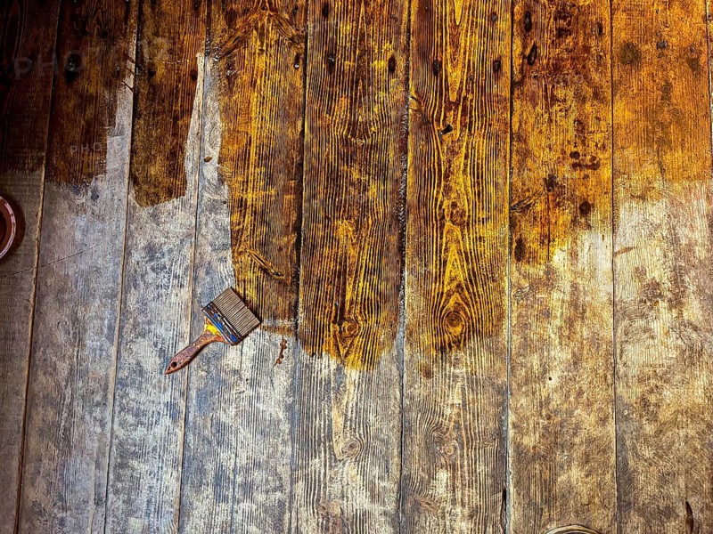 Wooden floor being stained, with a paintbrush resting on the planks