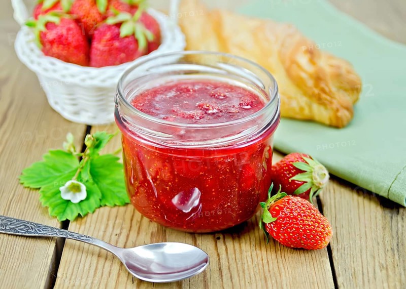Strawberry jam in a glass jar, layered bun, strawberry, napkin, spoon on a wooden boards background