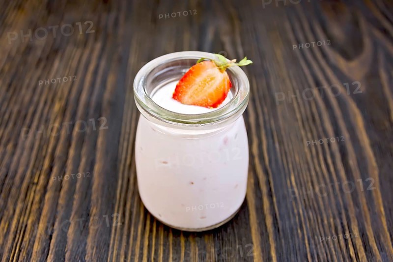 Yogurt with strawberries in a glass jar on a wooden boards background
