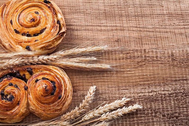 Golden wheat ears fresh-baked buns with raisins on oaken wooden board food and drink concept