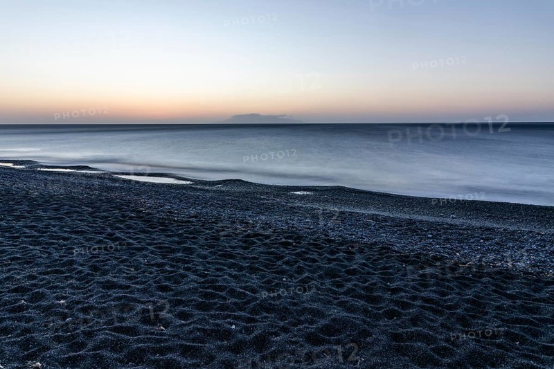 Morning atmosphere, sunrise over the sea, view from the lava beach to the island of Anafi, long exposure, Kamari, island of Santorini, Cyclades, Greece, Europe