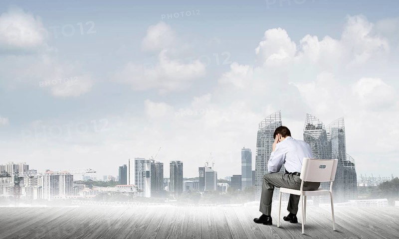 Businessman sitting on an office chair with his back, thinking and holding his head