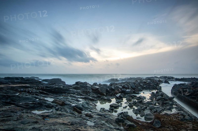 Beach, with lava rocks and vegetation, view of the sea in the evening at sunset. Landscape with clouds in Induruwa, Bentota Beach, Sri Lanka, India, Asia