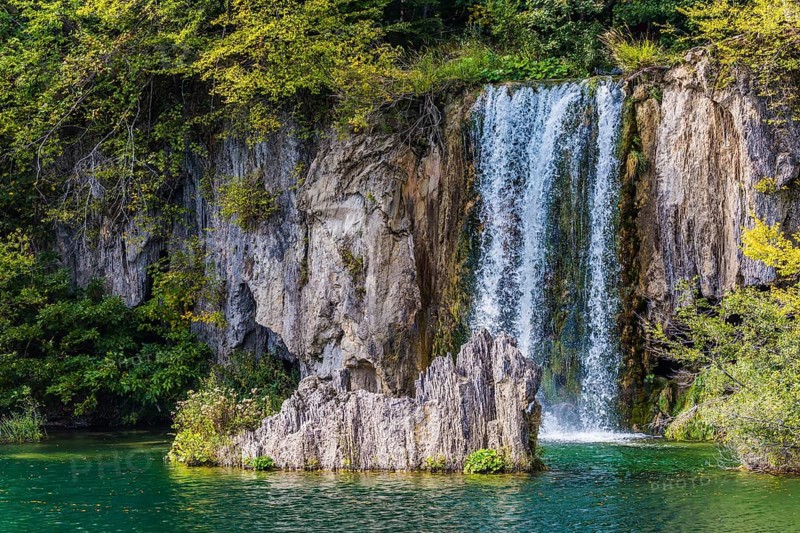 Charming little waterfall with a vertical ledge. Cascading Plitvice lakes in Croatia on a cloudy warm day. The concept of ecological, active and phototourism