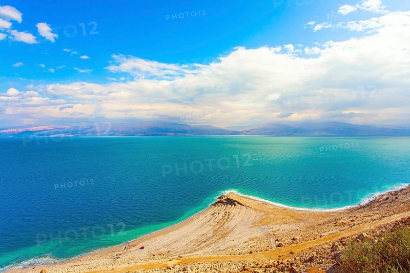 The smooth surface of the very salty sea water reflects the sky and clouds. Low winter clouds are reflected in the green sea water. Israel. Legendary Dead Sea