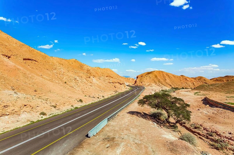 Straight as an arrow the road crosses the hills. Dry waterless hills of yelloy and beige clay. Judean desert on the shores of the Dead Sea. Israel. Shooting from drone