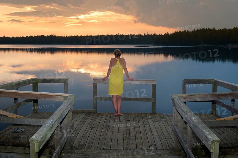 Young woman standing on a pier and admired the sunset on a lake in Småland, Sweden, Europe