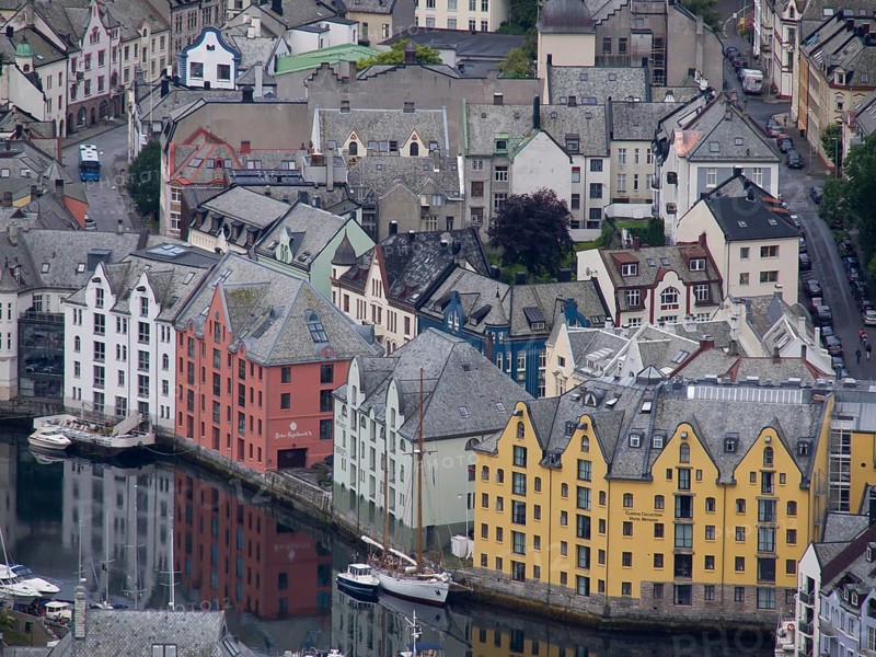 Colourful buildings on the harbour are reflected in the water. Historic architecture and Scandinavian style dominate the scene, alesund, norway