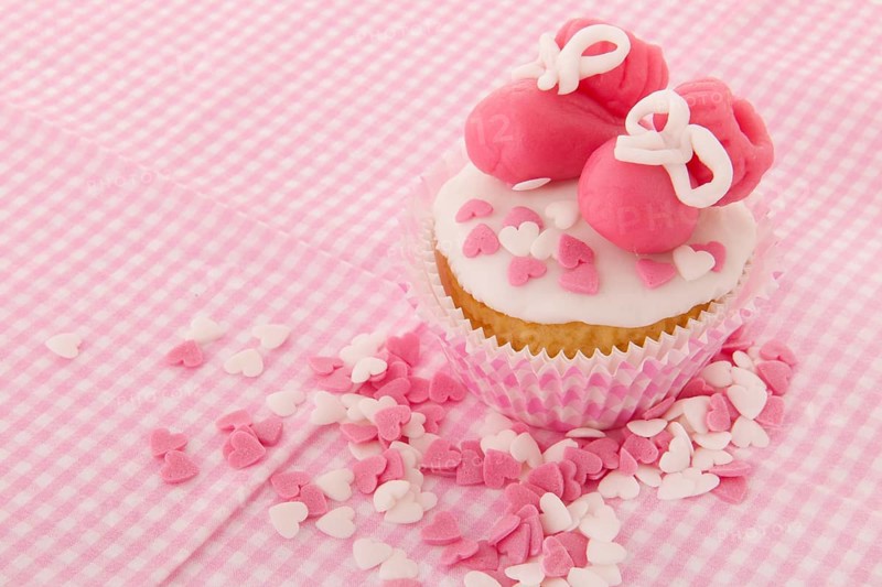 Pink cupcake with baby shoes and hearts