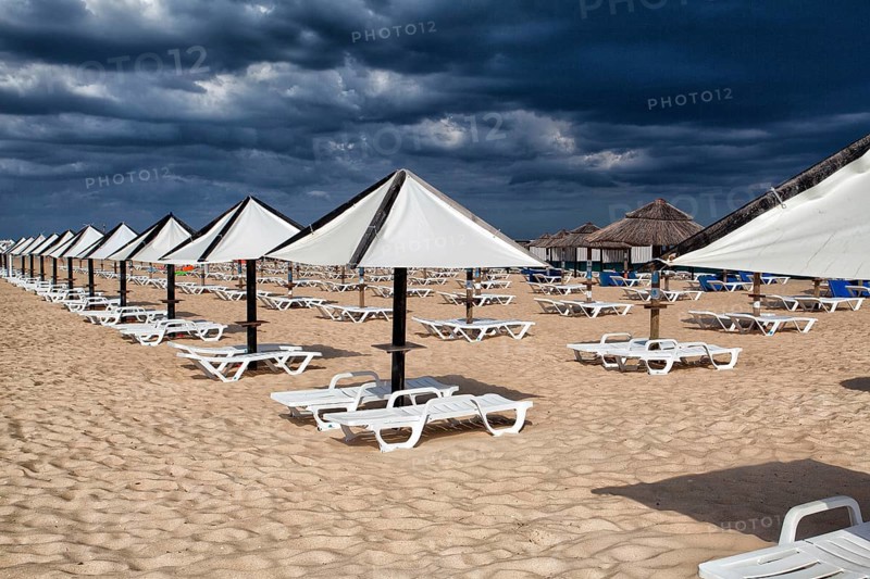 Different parasols and sun loungers on the empty beach on Tavira island before storm, Algarve. Portugal