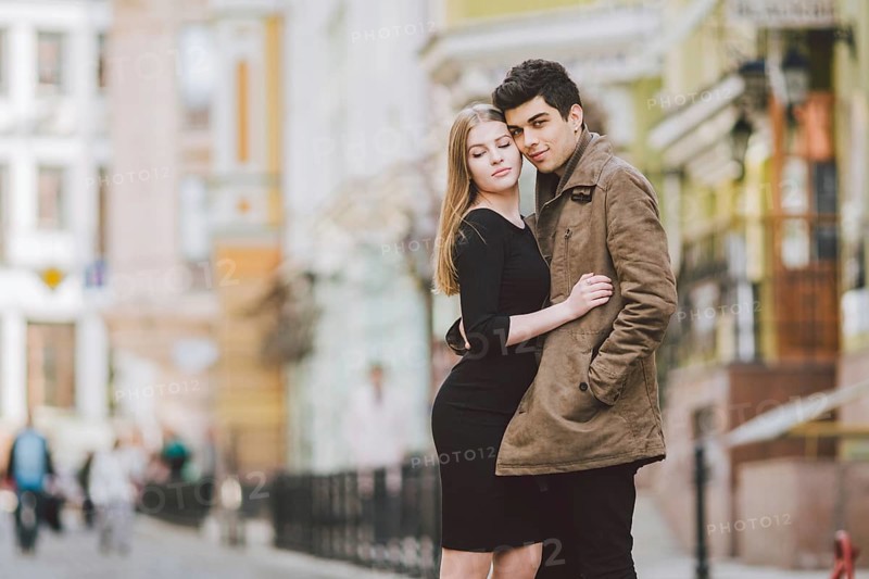 Urban modern young love couple walking romantic talking talking, holding hands on a date. Young multicultural Turkish brunette and Caucasian couple on old european street. Autumn spring weather