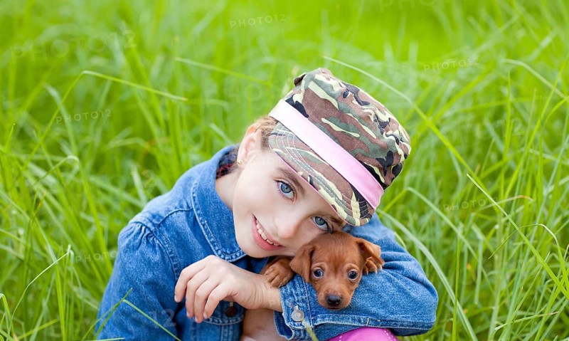 Little girl with pet puppy mascot mini pinscher in outdoor green grass