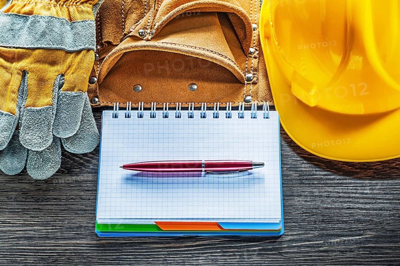Notepad pen tool belt safety gloves hard hat on wooden board
