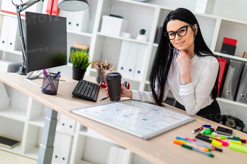 A young girl with glasses, wearing a white blouse and black trousers, works in the office. The girl has long straight black hair. photo with depth of field
