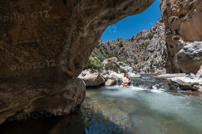 Preveli Beach, at the end of the Kourtaliotiko Gorge, South Coast, Crete, Greek Islands, Greece, Europe. young man sitting in the river, Europe
