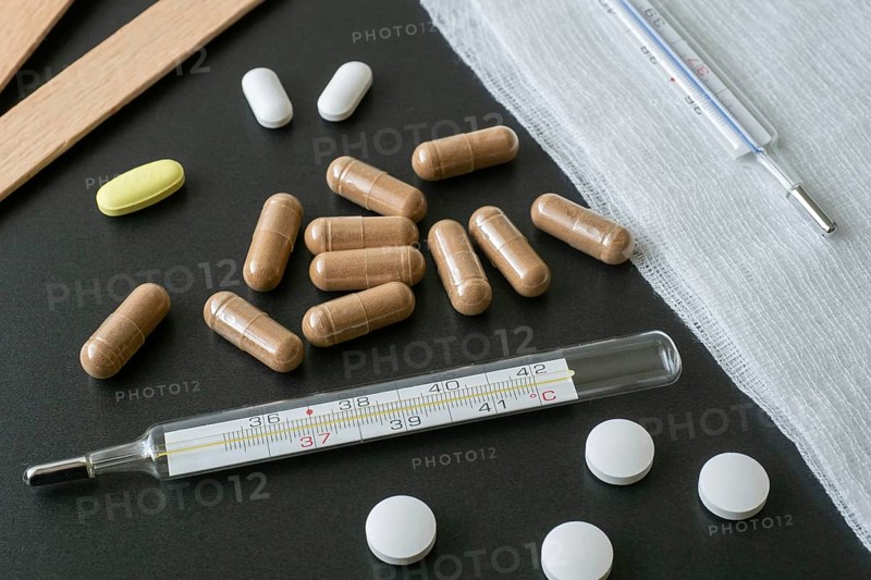 Traditional medical thermometer for measuring body temperature. Pills and medicaments on background. High body temperature