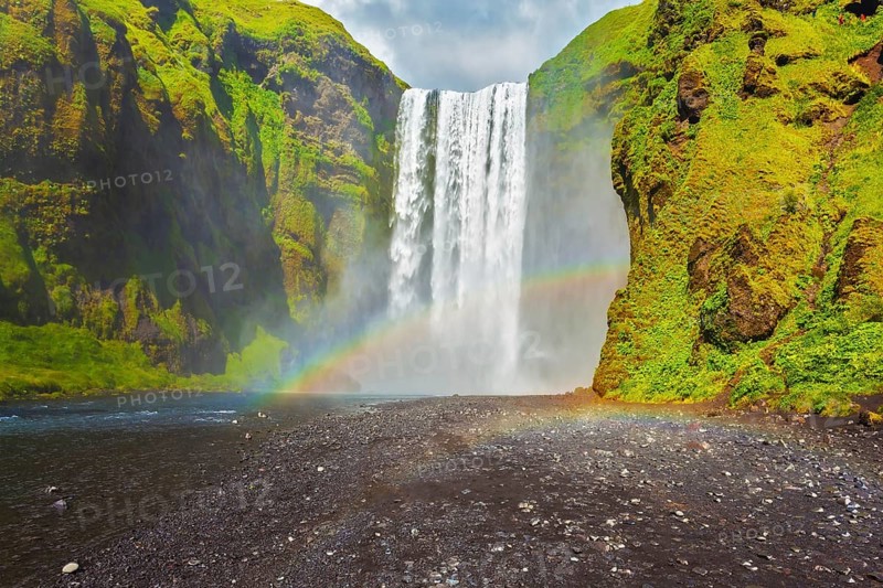 Picturesque huge rainbow appears in the water mist. The most popular waterfall in Iceland - Skogafoss. Water rushes down with a crash, forming a cloud of mist