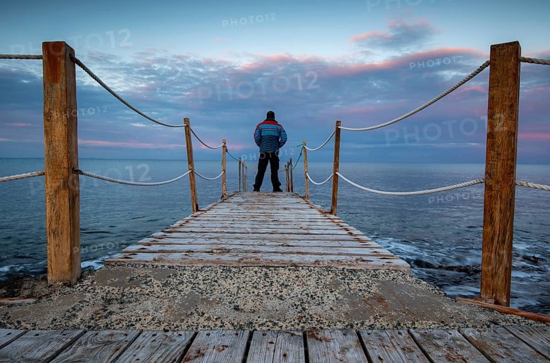 Person standing at the edge of a wooden pier in the sea at sunrise, People active outdoors enjoy ocean. Protaras Cyprus